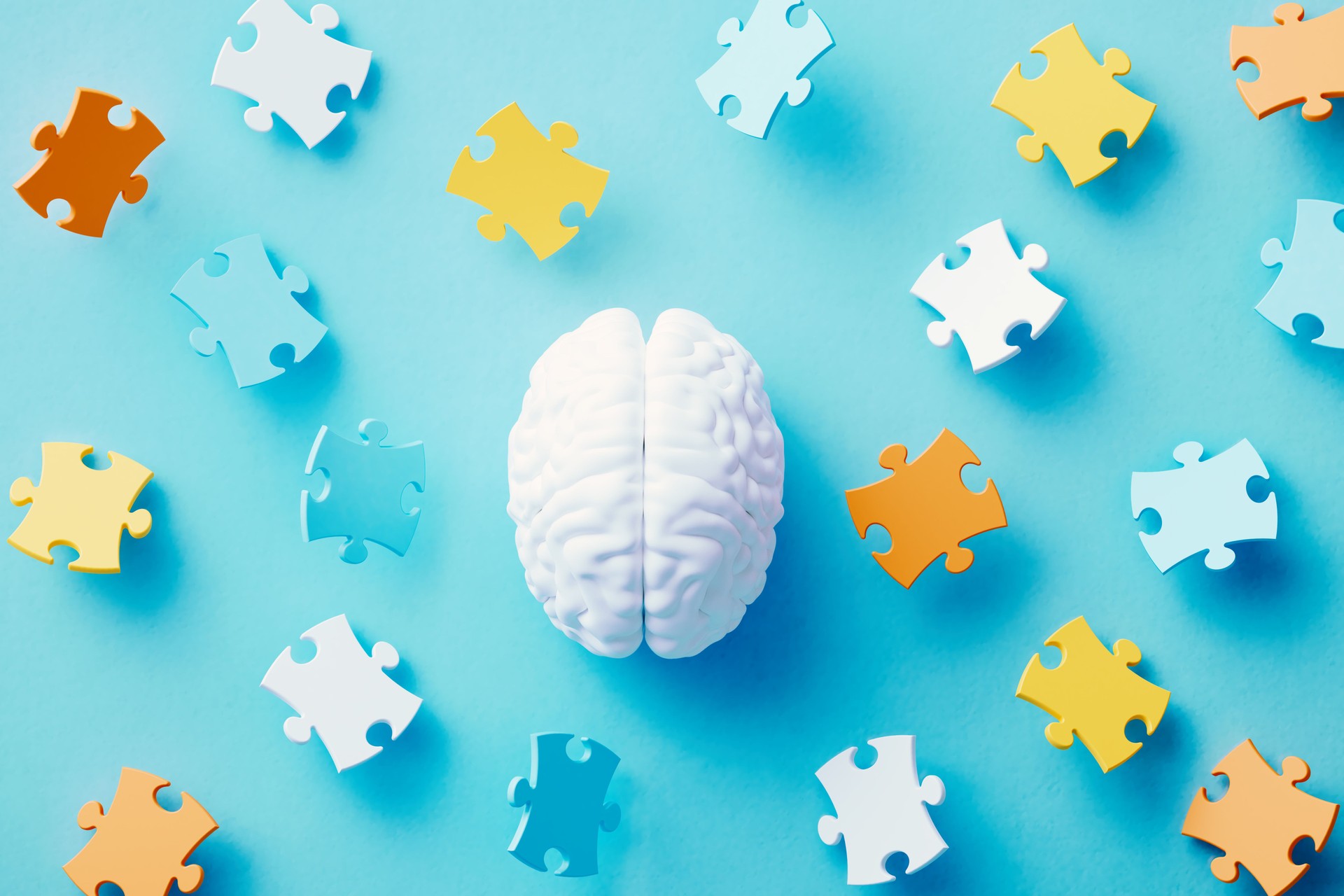 White Human Brain Surrounded By Colorful Jigsaw Puzzle Pieces On Blue Background